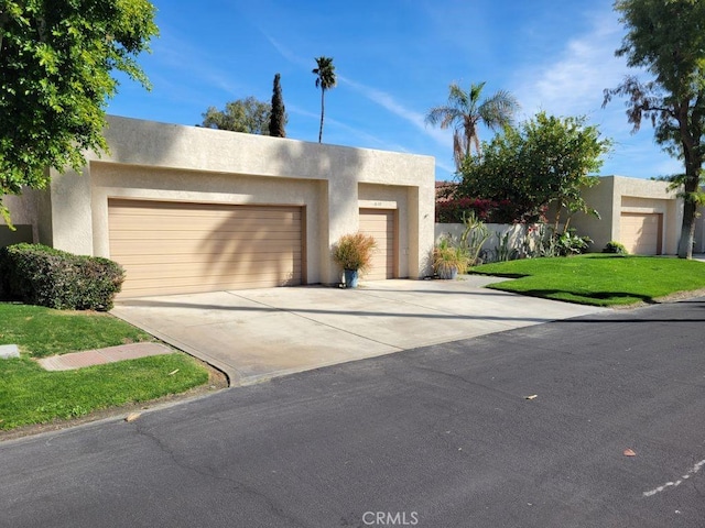 pueblo-style home featuring stucco siding, driveway, a garage, and a front yard