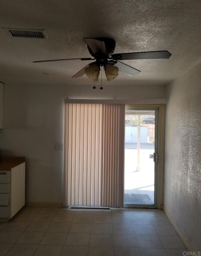 spare room featuring baseboards, a textured wall, a textured ceiling, a ceiling fan, and visible vents