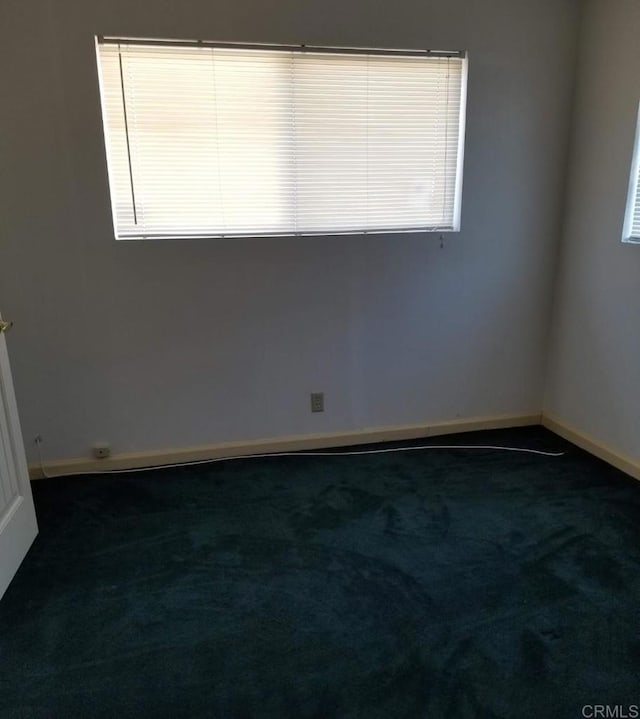 unfurnished room with baseboards and dark colored carpet