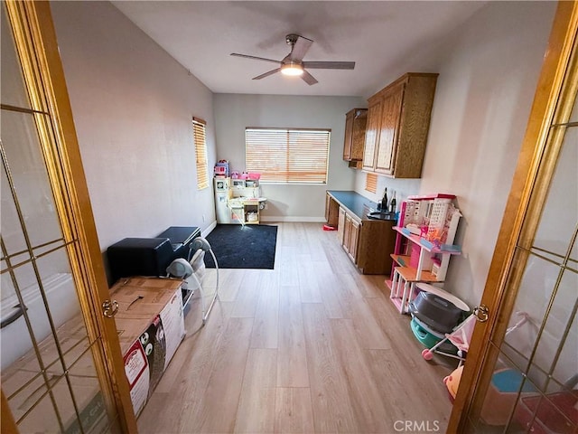 interior space featuring baseboards, brown cabinets, a ceiling fan, and light wood-style floors