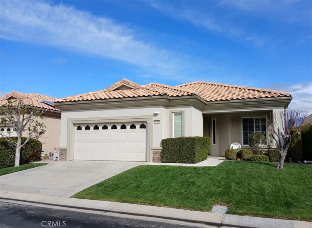 mediterranean / spanish home featuring stucco siding, driveway, a front yard, an attached garage, and a tiled roof