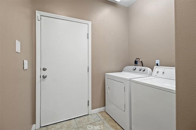 clothes washing area featuring washing machine and dryer, a skylight, light tile patterned floors, baseboards, and laundry area