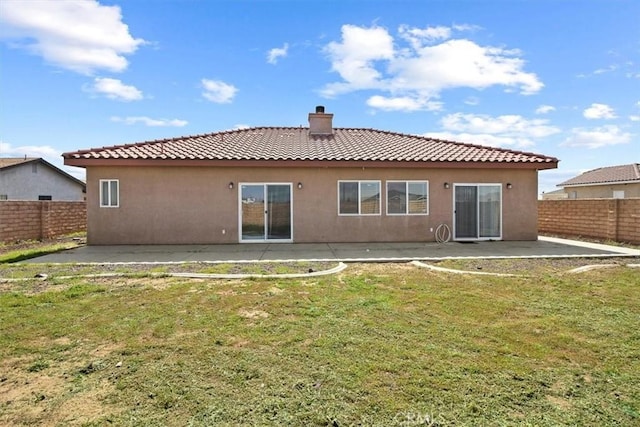 back of house featuring a tile roof, a fenced backyard, a yard, a chimney, and a patio area