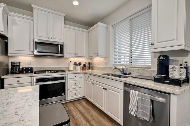 kitchen with light wood-type flooring, recessed lighting, white cabinets, a sink, and appliances with stainless steel finishes