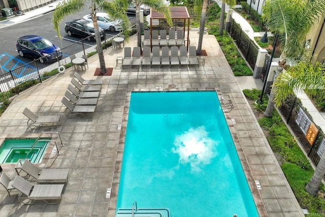 pool with a patio, a community hot tub, and fence