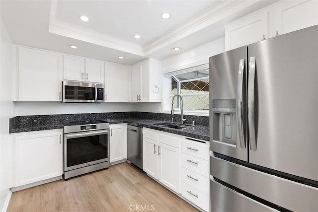 kitchen with a sink, a tray ceiling, white cabinetry, stainless steel appliances, and light wood-style floors