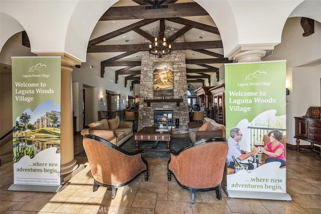 living room featuring beamed ceiling, stone tile flooring, a chandelier, decorative columns, and a fireplace