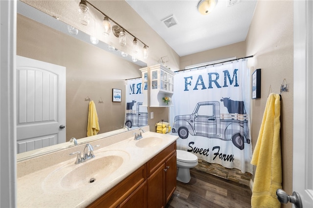 bathroom with double vanity, toilet, wood finished floors, and a sink