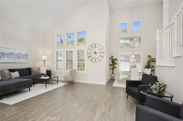 living area with baseboards, light wood-style floors, and high vaulted ceiling