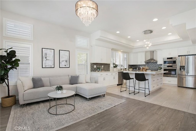 living area with a tray ceiling, recessed lighting, light wood-style floors, and a chandelier