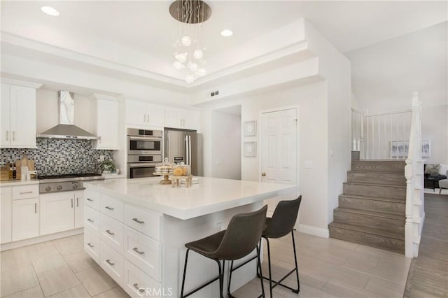 kitchen featuring backsplash, light countertops, a raised ceiling, stainless steel appliances, and wall chimney exhaust hood