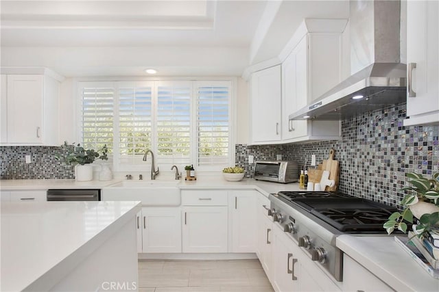 kitchen featuring a sink, tasteful backsplash, white cabinetry, stainless steel gas stovetop, and wall chimney exhaust hood