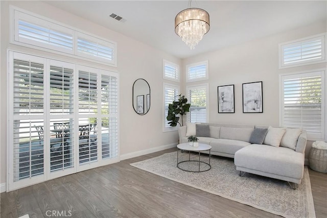 living area featuring visible vents, a healthy amount of sunlight, wood finished floors, and an inviting chandelier