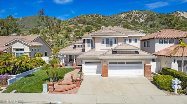 view of front of property featuring driveway, brick siding, stucco siding, a tiled roof, and a mountain view