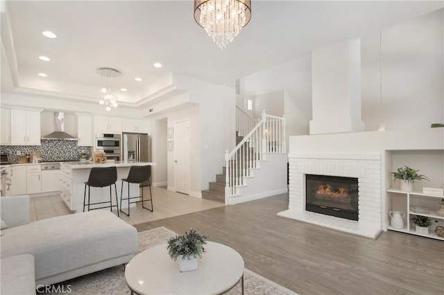 living area featuring stairs, a tray ceiling, light wood-style flooring, and an inviting chandelier