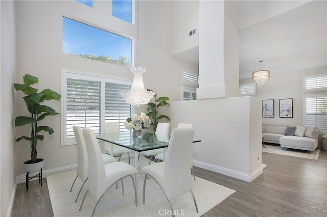 dining room featuring visible vents, wood finished floors, a high ceiling, baseboards, and a chandelier