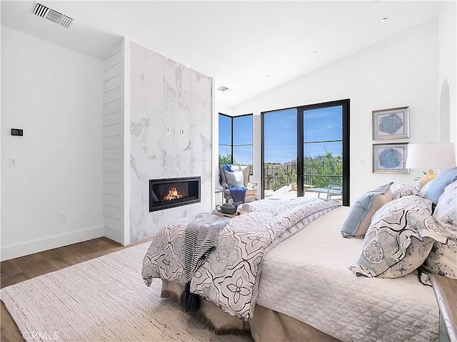 bedroom featuring visible vents, wood finished floors, a premium fireplace, lofted ceiling, and access to exterior