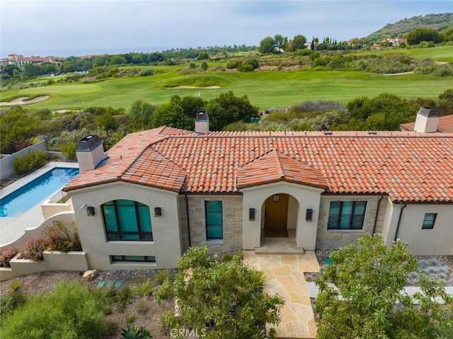 back of house featuring view of golf course, a tiled roof, stone siding, and a chimney