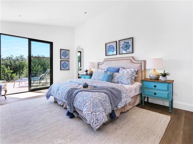 bedroom with baseboards, vaulted ceiling, wood finished floors, arched walkways, and access to outside