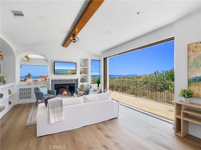 living area featuring visible vents, vaulted ceiling with beams, built in features, wood finished floors, and a glass covered fireplace