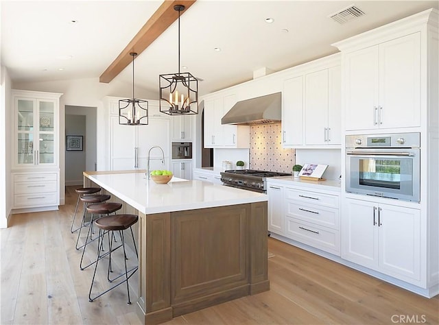 kitchen with range hood, lofted ceiling with beams, light wood-type flooring, and stainless steel appliances