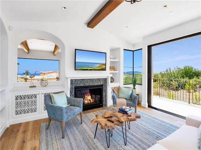 living room with built in features, wood finished floors, vaulted ceiling with beams, arched walkways, and a tiled fireplace