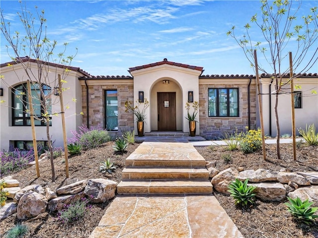 mediterranean / spanish home featuring stucco siding, stone siding, and a tile roof