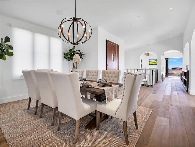 dining space with recessed lighting, arched walkways, an inviting chandelier, light wood finished floors, and baseboards