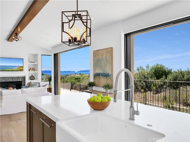 kitchen with built in shelves, light wood-style flooring, a sink, an inviting chandelier, and a fireplace