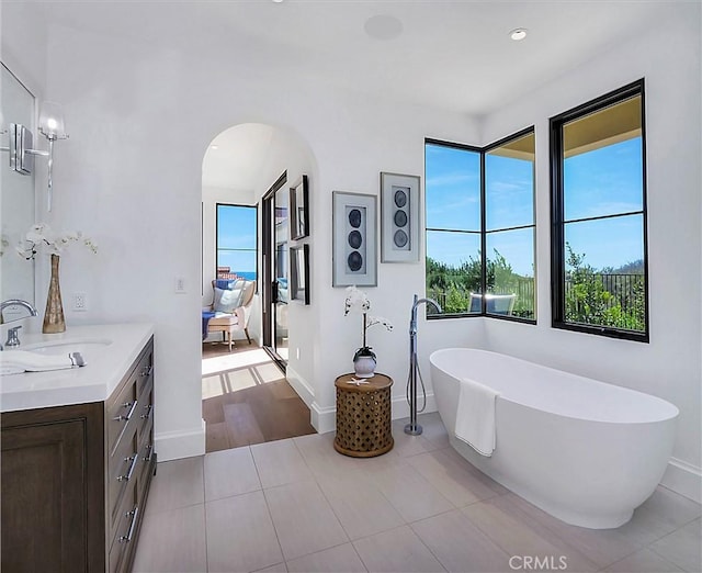 ensuite bathroom with vanity, tile patterned floors, a healthy amount of sunlight, and a freestanding bath