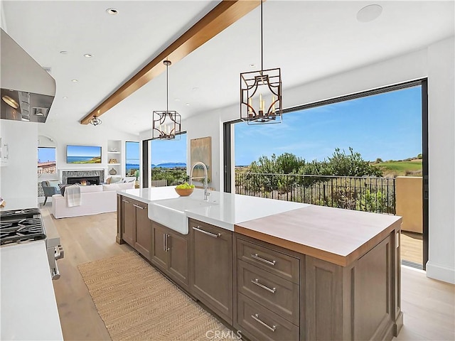 kitchen featuring a center island with sink, beam ceiling, a sink, light countertops, and light wood-style floors