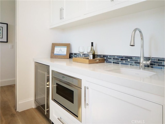 kitchen with light wood finished floors, backsplash, wine cooler, white cabinetry, and a sink