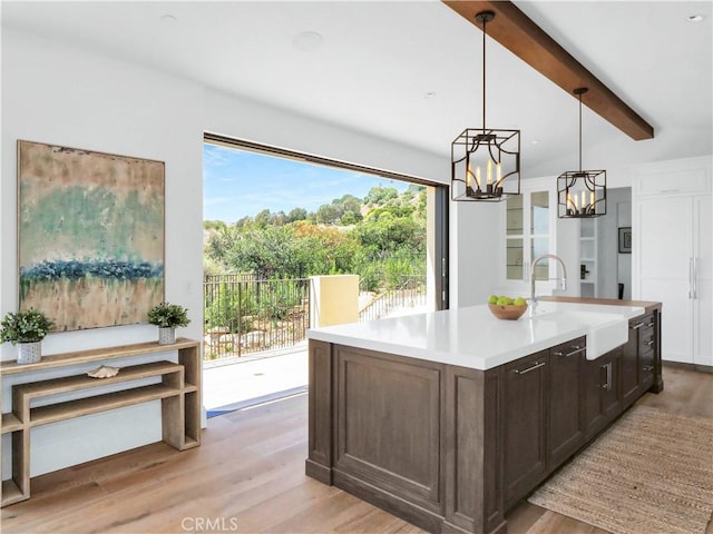 kitchen with light wood finished floors, a sink, light countertops, beamed ceiling, and a chandelier