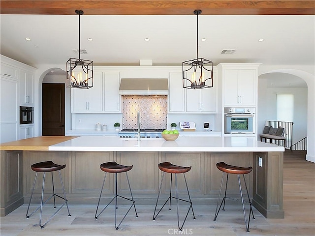 kitchen featuring oven, visible vents, arched walkways, and ventilation hood