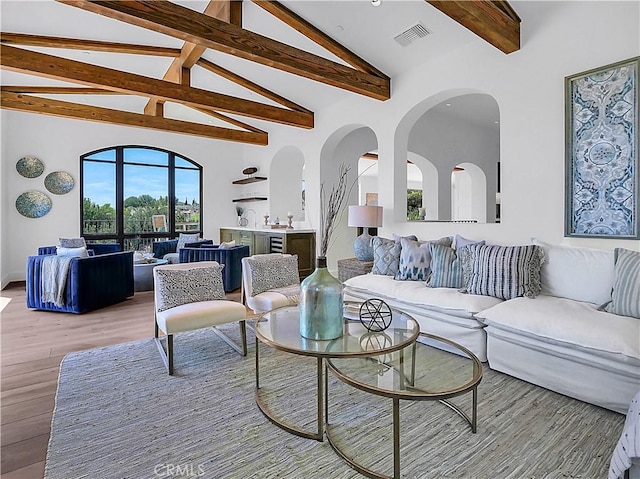 living room featuring beam ceiling, visible vents, light wood-style flooring, and high vaulted ceiling