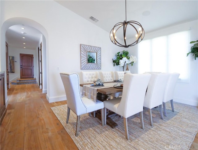 dining space with visible vents, baseboards, arched walkways, light wood-style floors, and a notable chandelier