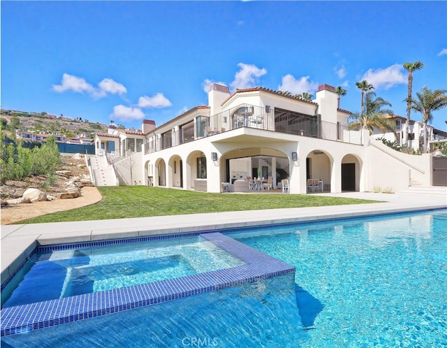 back of property with a lawn, stucco siding, a chimney, a balcony, and a patio