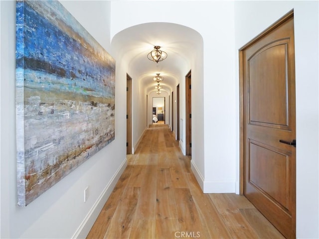 hallway featuring light wood-style flooring, baseboards, and arched walkways