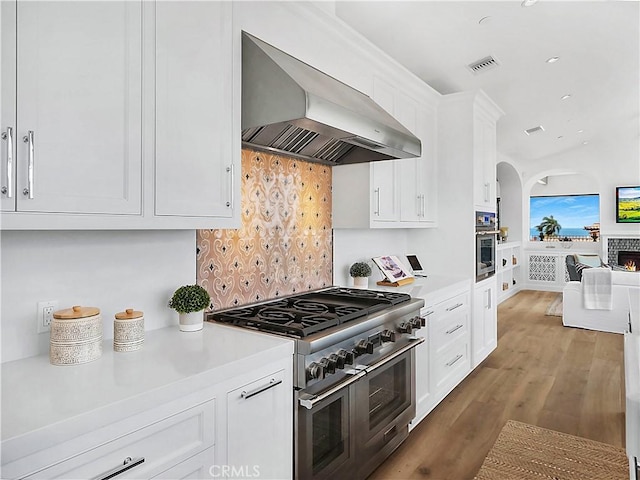 kitchen featuring visible vents, light countertops, appliances with stainless steel finishes, white cabinetry, and wall chimney exhaust hood