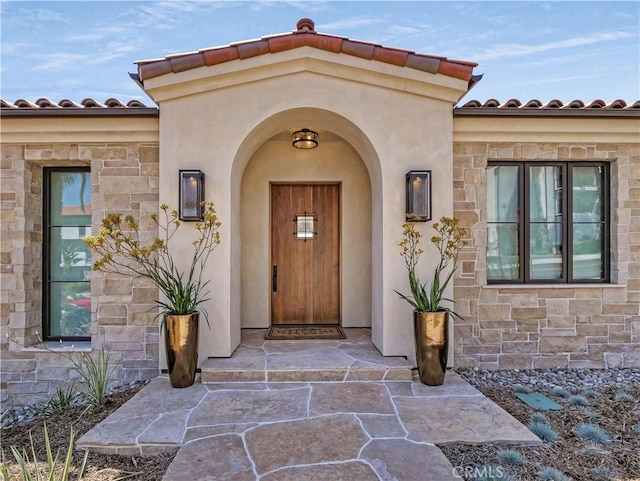 property entrance with stucco siding, stone siding, and a tile roof