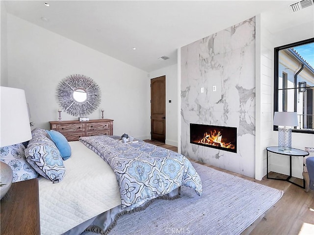 bedroom with a premium fireplace, visible vents, and wood finished floors