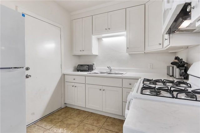 kitchen featuring white appliances, light countertops, under cabinet range hood, and a sink