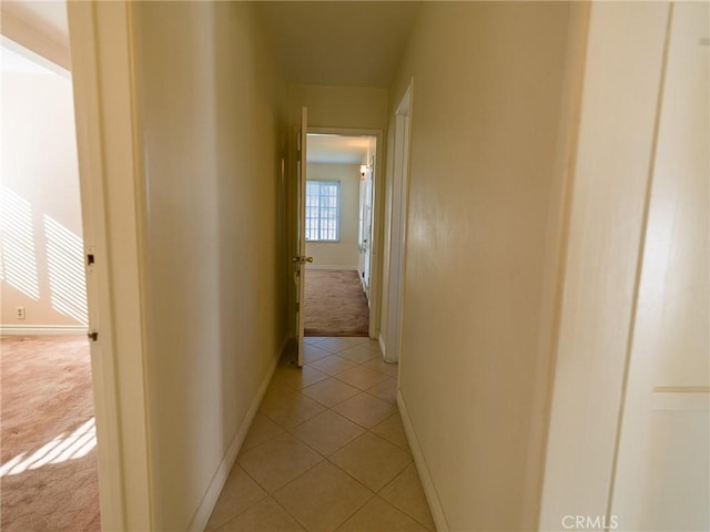 corridor with light tile patterned floors, baseboards, and light carpet