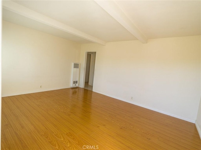 spare room with baseboards, beam ceiling, and light wood-style floors