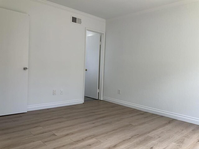 empty room featuring crown molding, baseboards, visible vents, and wood finished floors