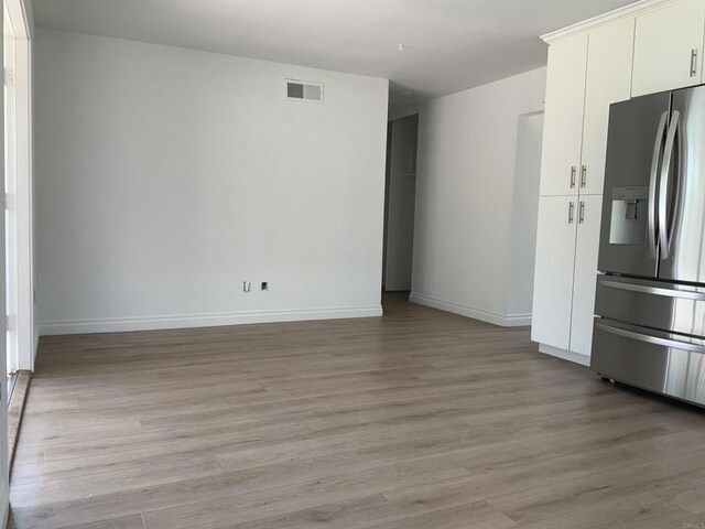 interior space featuring white cabinets, stainless steel fridge with ice dispenser, light wood-style flooring, baseboards, and visible vents
