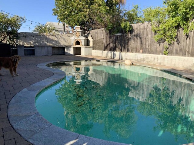 view of swimming pool featuring a patio, a fireplace, a fenced backyard, and a fenced in pool