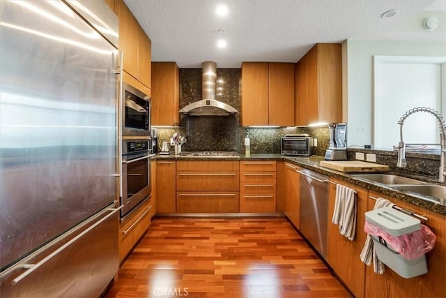 kitchen with brown cabinetry, light wood finished floors, appliances with stainless steel finishes, and wall chimney range hood