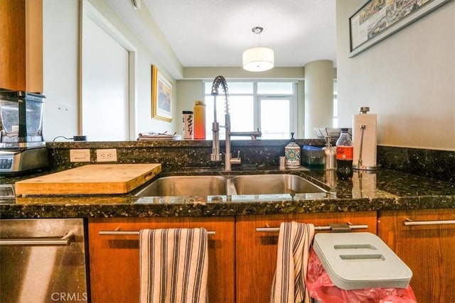 kitchen featuring dark stone countertops, pendant lighting, brown cabinets, and a sink