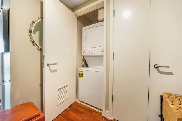 clothes washing area with laundry area, stacked washer / drying machine, visible vents, and dark wood-style flooring